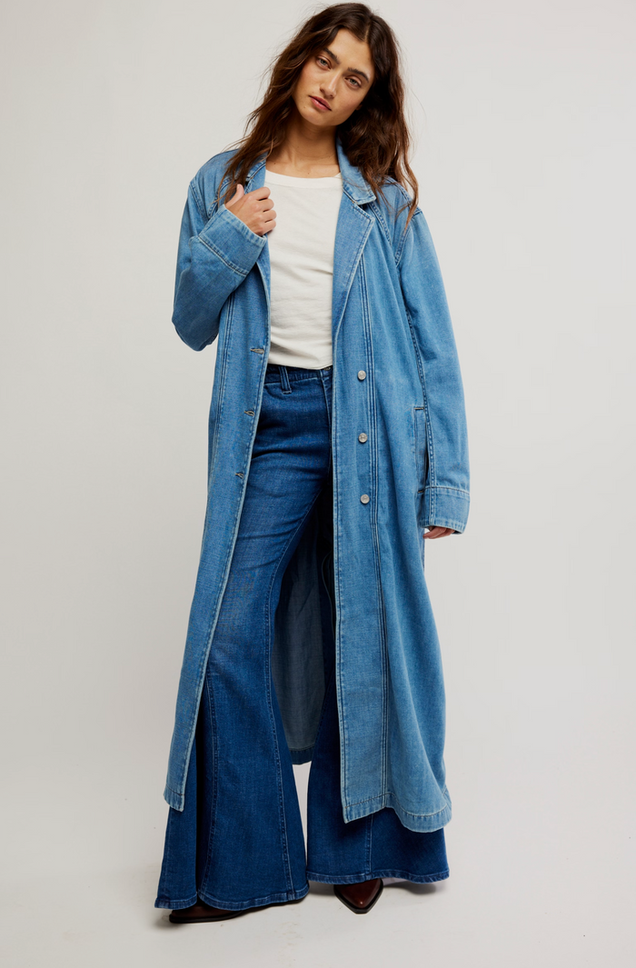 Woman wearing a long denim jacket and jeans on a plain background