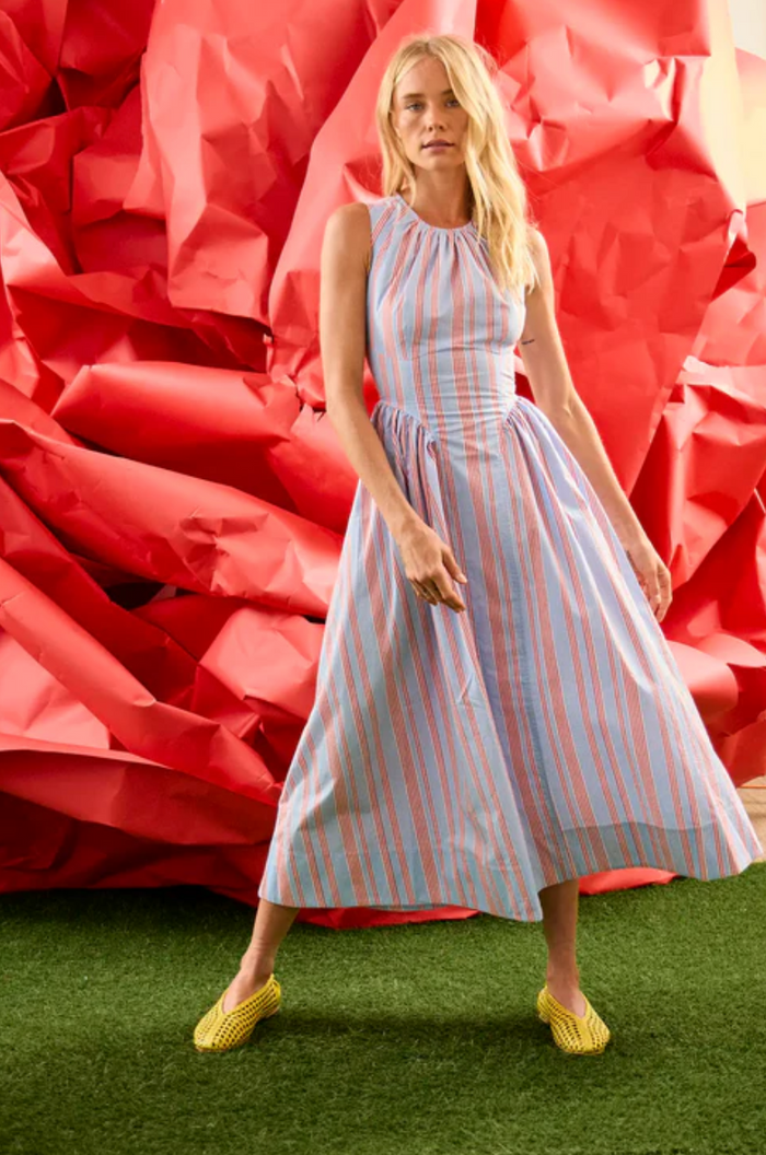 Woman in a striped dress standing in front of large red flowers on grass