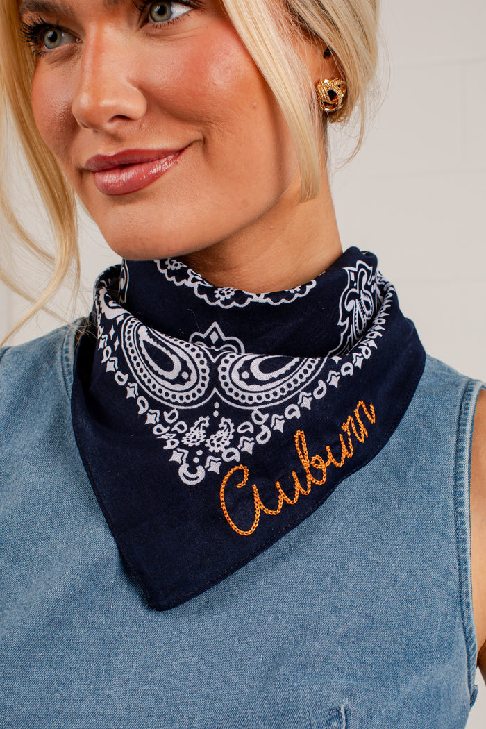 A close-up of a woman wearing a navy blue bandana with a white paisley pattern and the word 'Cubson' embroidered in orange on the front. She is wearing a light blue denim top.