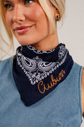 A close-up of a woman wearing a navy blue bandana with a white paisley pattern and the word 'Cubson' embroidered in orange on the front. She is wearing a light blue denim top.
