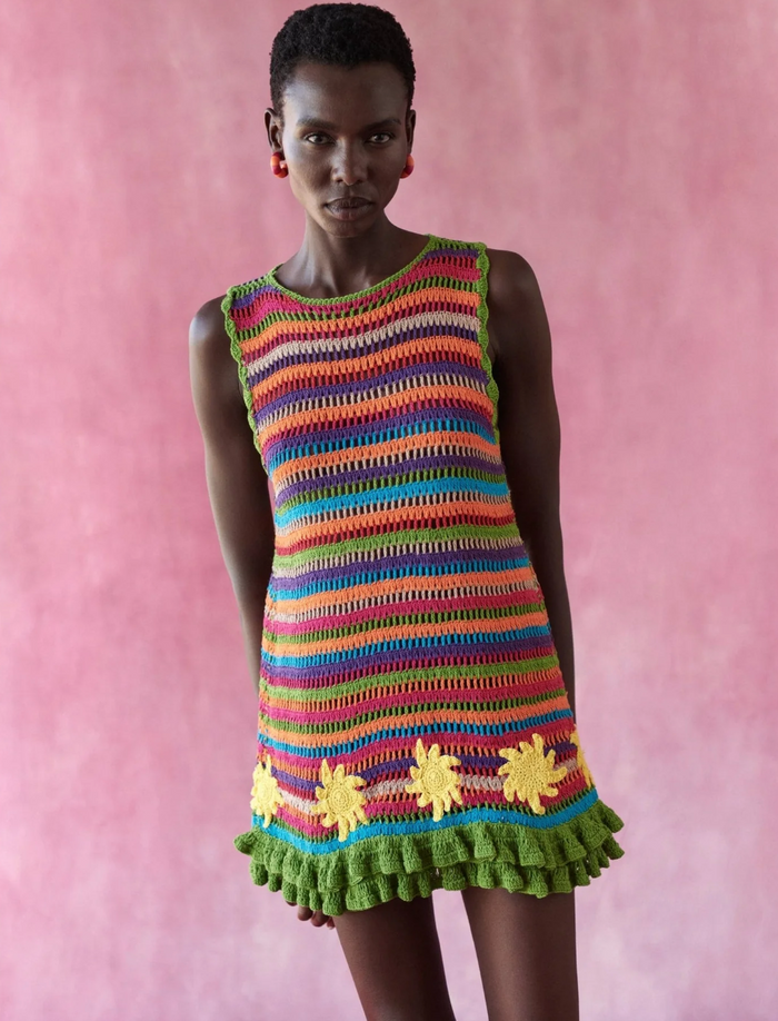 Model wearing a colorful striped dress with floral details against a pink background