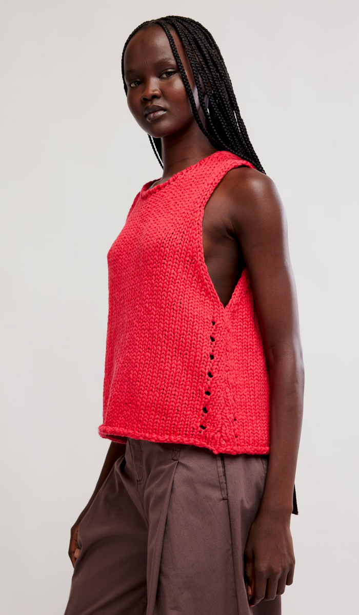 Woman wearing a sour sweet knitted vest with button details on a plain background