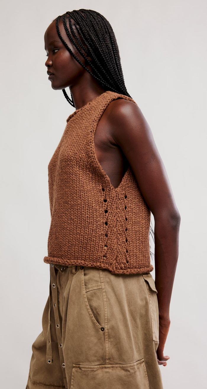 Woman wearing a emperador knitted vest and beige pants against a plain background