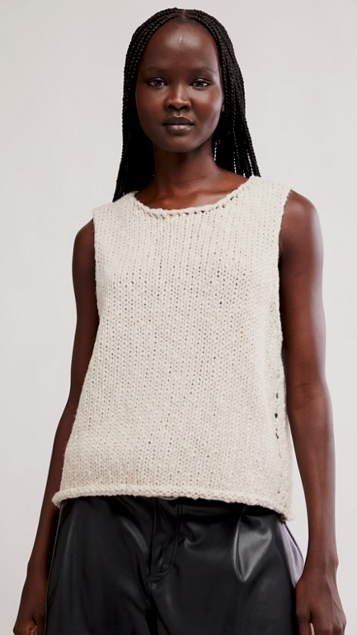 Woman wearing a tea knitted sleeveless top against a plain background