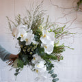 Bouquet of white flowers and greenery held by a person against a light background