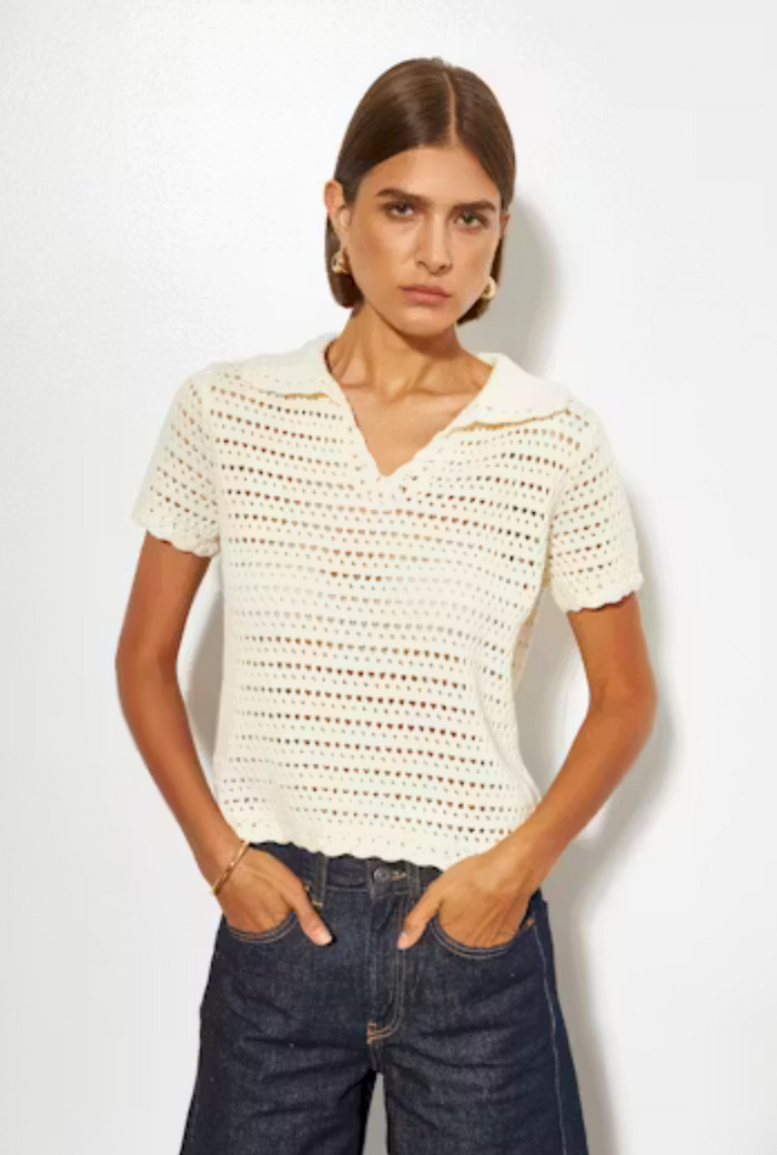 Woman wearing a white crochet top and dark jeans against a plain background