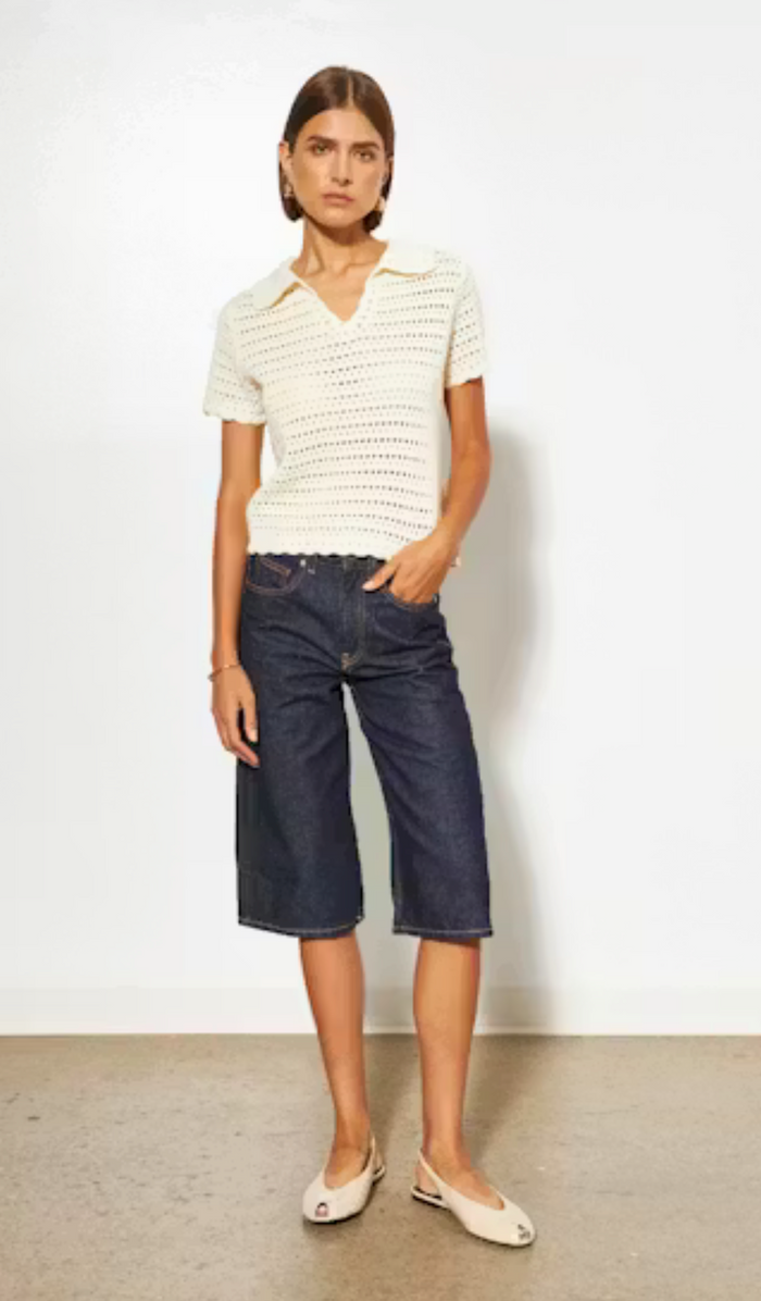 Woman wearing a white knit top and dark blue jeans against a plain background