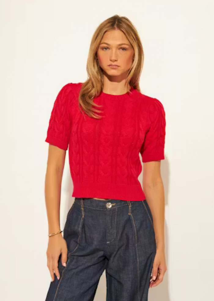 Woman wearing a red knitted top and blue jeans against a white background