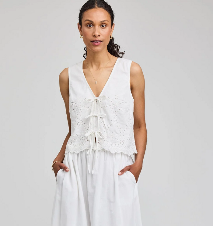 Woman wearing a white sleeveless top with ruffle details on a gray background