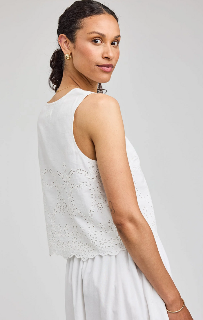 Woman wearing a white sleeveless top with cut-out details on a light gray background