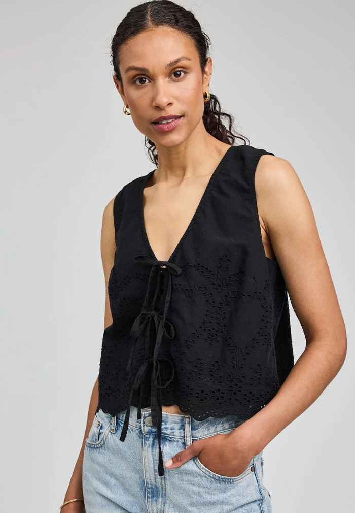 Woman wearing a black sleeveless top with eyelet details on a gray background
