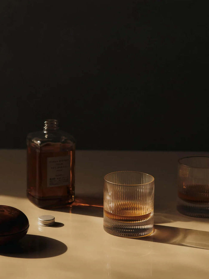 Ripple Tumbler Glasses with whiskey and a bottle in soft lighting on a table.