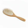 A wooden hairbrush with a light natural wood handle and head, beige bristles, and a white inner pad, shown on a plain white background.