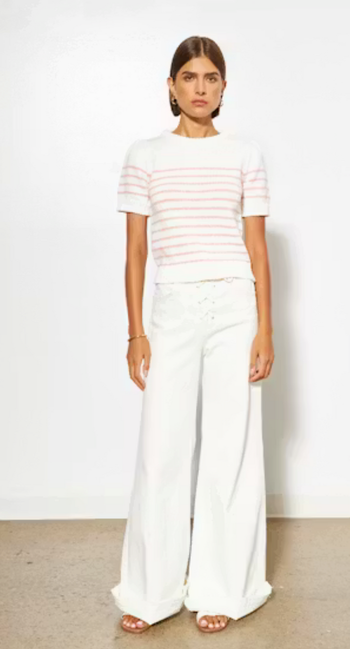 Woman wearing a striped shirt and white pants against a plain background