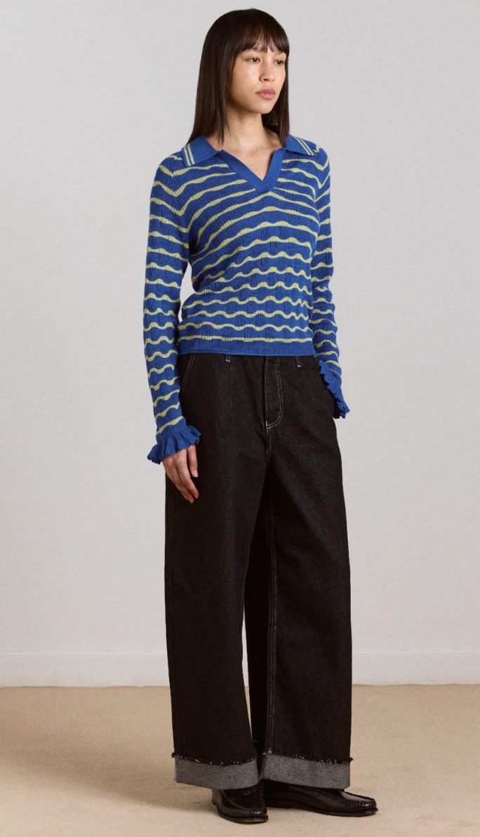 Person wearing a blue and white patterned sweater with black pants on a plain background