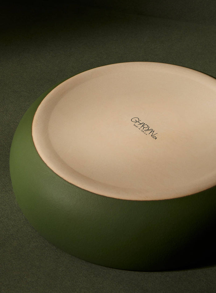 Underside of green ceramic bowl with a visible brand logo on a dark green background