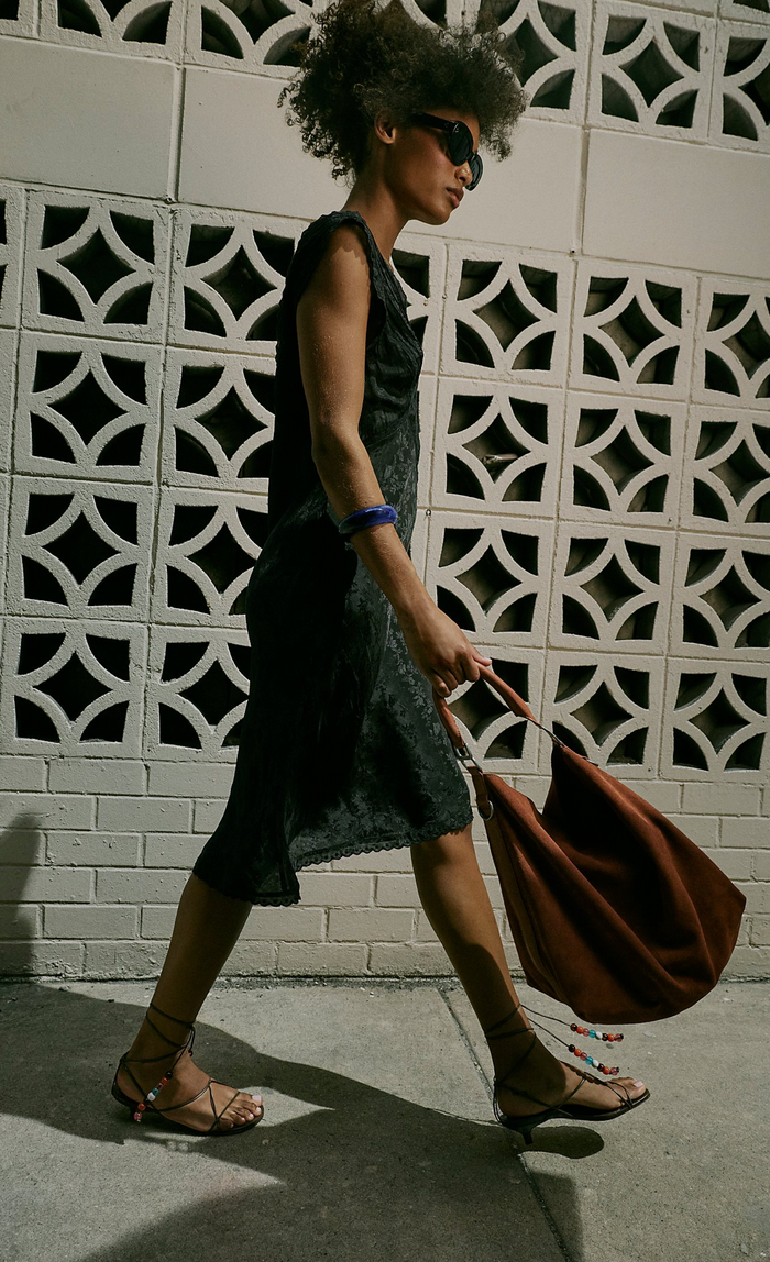 Woman walking with a brown bag against a patterned wall.