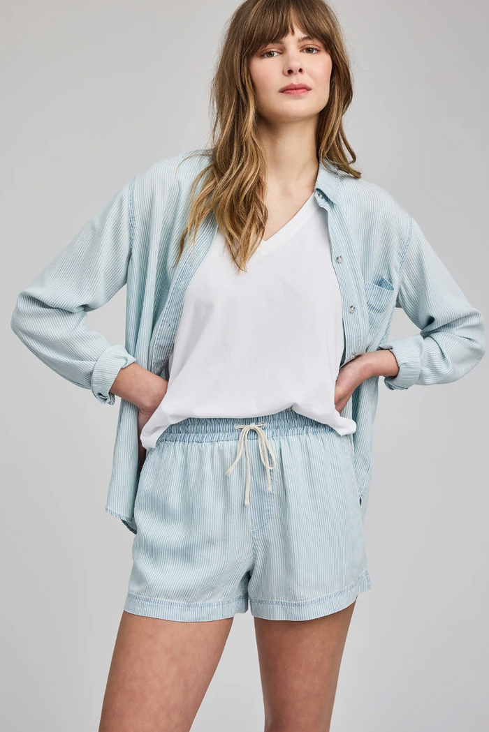Woman wearing a light blue shirt and shorts set on a gray background
