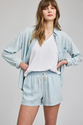 Woman wearing a light blue shirt and shorts set on a gray background