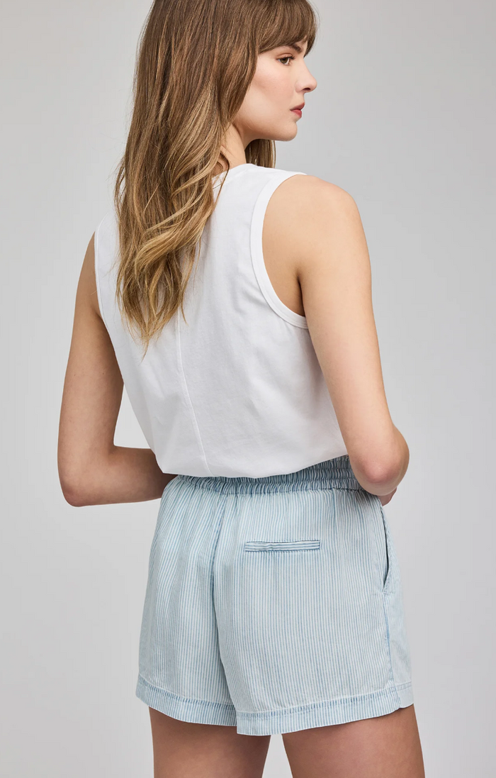 Woman wearing a white sleeveless top and light blue striped shorts on a plain background