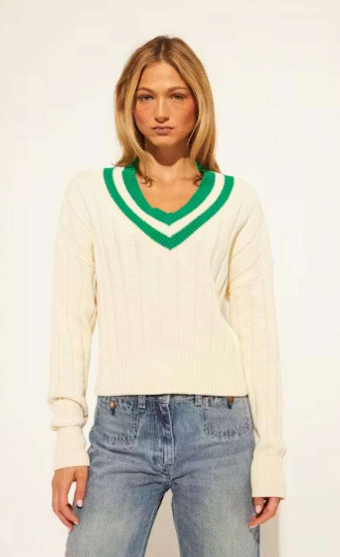 Woman wearing a cream sweater with green trim and blue jeans on a white background