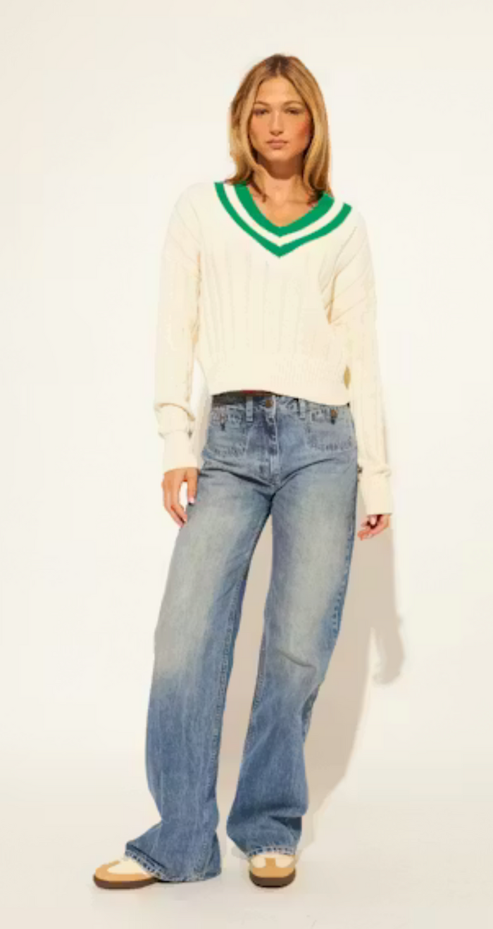 Woman wearing a white sweater with green trim and blue jeans on a white background