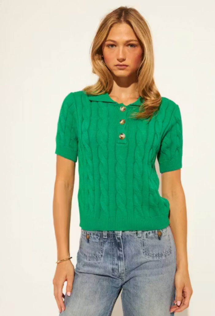 Woman wearing a green short-sleeve top with a collar and blue jeans on a white background