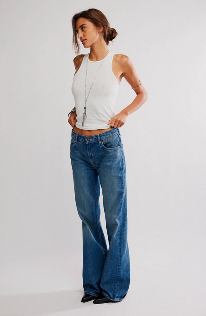 Woman wearing a white sleeveless top and blue jeans on a plain background